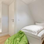 Bedroom with sloped ceiling, white bed, and green bean bag on wooden floor.