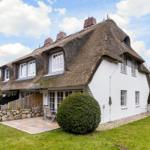 A white house with a thatched roof and terrace in the garden.