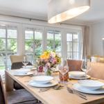 Dining table with chairs and floral decoration by windows.