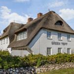 Weiße Hütte mit Strohdach und Gartenzaun. Schriftzug GREEN TEFT auf Fassade.