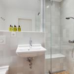 Badezimmer mit Dusche, Waschbecken und Toilette. Fliesenwand und Spiegel.