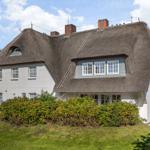 Traditionelles Haus mit Strohdach und weißen Wänden, umgeben von Grünflächen und Sträuchern.