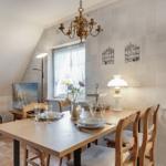 Esszimmer mit Holztisch, Stühlen und Fenstern mit weißen Vorhängen.
