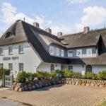 Ein großes Haus mit Strohdach und weißen Wänden. Vorgarten mit Steinmauer und Pflanzen.