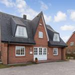 Red brick house with white windows and dark roof under blue sky.