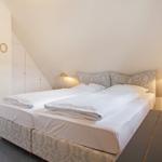 Bedroom with double bed, nightstand, and lamp under sloped ceiling.
