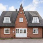 Red brick house with white windows and dormers under blue sky.