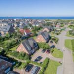 Aerial view of a coastal village with houses, gardens, and the sea in the background.