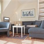 Living room with sofa, armchair, table, and wall art. Patio door and staircase visible.