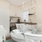 Dining area with white table and chairs, kitchenette, and chandelier.