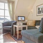 Living room with sofa, armchair, and TV. Windows with balcony view.