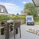 Terrasse mit Tisch, Stühlen und Strandkorb. Hinterhof mit Hecke und Steinbeete.