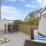 Terrasse mit Strandkorb, Tisch und Stühlen. Hinterhof mit Holzzaun und Pflanzen.