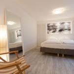 Schlafzimmer mit Bett, Spiegel und Stehlampe. Wandbild und Holzboden.