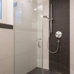 Dusche mit Glaswand, dunkler Wandverkleidung und Duschbrause