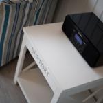 Schwarzener Radio auf weißem Tisch neben gestreiftem Sofa.