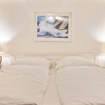 Zwei Betten mit weißen Bettwäschen, zwei Nachttische mit Lampen und ein Bild an der Wand.