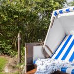 Strandkorb mit blau-weißem Streifenmuster und Ankermotivdecke im Garten.