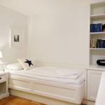Ein Schlafzimmer mit weißem Bett, Nachttisch und Bücherregal.