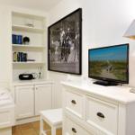 Schlafzimmer mit weißem Schrank, Fernseher und Wandbild.