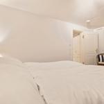 Schlafzimmer mit weißem Bett, Nachttischlampe und Stuhl mit Kissen.