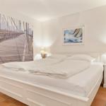 Schlafzimmer mit weißem Bett, Wandbild einer Brücke und zwei Nachttischen mit Lampen.