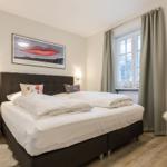 Schlafzimmer mit Doppelbett, Fenster, Vorhang und Stuhl.