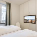 Schlafzimmer mit Bett, Fenster und eingebauter TV-Anlage.
