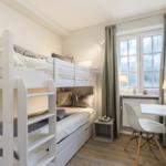 Zimmer mit Doppelstockbett, Schreibtisch und Fenster mit Vorhängen.