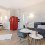 Wohn- und Essbereich mit grauem Sofa, rotem Kühlschrank und Holzboden.