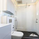 Modern shower with glass enclosure, sink, and toilet in white color scheme.