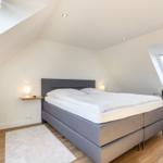 Bedroom with sloped ceilings, bed, desk, and plant.