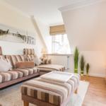 Wohnzimmer mit Sofa, Couchtisch und Fernseher. Wandbilder und Pflanzen sorgen für eine gemütliche Atmosphäre.