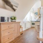 Eingangsbereich mit Holzschrank, Treppe und Blick in die Küche.