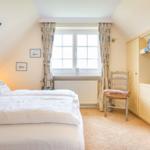 Schlafzimmer mit Doppelbett, Fenster, Stuhl und TV-Einbau