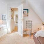 Schlafzimmer mit zwei Betten, Stuhl und Tür zum Anschlussraum.
