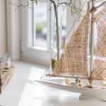 Ein Modellboot mit Segeln steht auf einer weißen Oberfläche. Im Hintergrund ist ein Fenster zu sehen.
