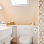 Badezimmer mit Waschbecken, Toilette und Dusche. Dachfenster und Mosaikfliesen.