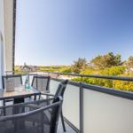Terrasse mit Tisch und Stühlen, Blick auf Grünflächen und Häuser.
