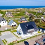 Haus mit dunklem Dach, umgeben von Grünflächen und dem Meer.