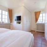 Room with double bed, TV, and two windows with curtains.