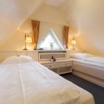 Two beds under sloped ceiling with window and nightstand.