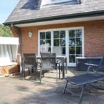 Terrace with lounge chair, table, chairs, and beach cabana in front of red brick house.