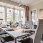Dining table with chairs, windows, and wall art in dining room.