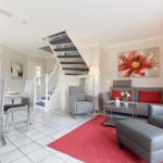 Living and dining area with staircase, sofa, armchairs, and red rug.
