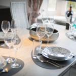 Dining table with dishes, glasses, and chairs. Window with view outside.