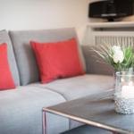 A gray sofa with red cushions and a table with a candle and flowers.