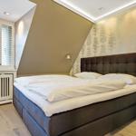Schlafzimmer mit Doppelbett, Fenster mit Jalousien und Wand mit Baum-Motivtapete.