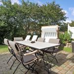 Terrasse mit Tisch, Stühlen und Liege unter Bäumen.