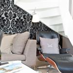 Sitzbereich unter Treppe mit Sofa und Ledersessel. Wand mit Muster, Flasche Champagner.